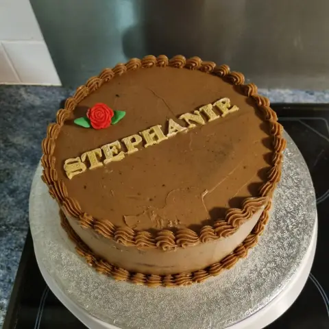 Gâteau au chocolat bordé de rosaces de crème, orné d'une rose rouge et d'un prénom en lettres dorées