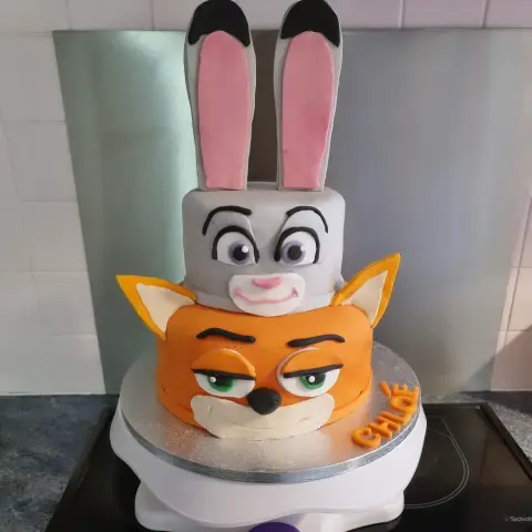 Gâteau à deux étages : tête de lapine grise aux longues oreilles roses sur une tête de renard orange, avec un prénom