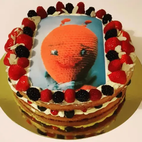 Gâteau nu garni de crème, fraises, framboises et mûres, avec l'image imprimée d'un doudou orange au crochet