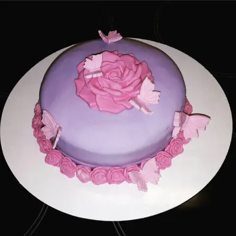 Gâteau mauve surmonté d'une grande rose rose, bordé de petites roses et entouré de papillons en sucre