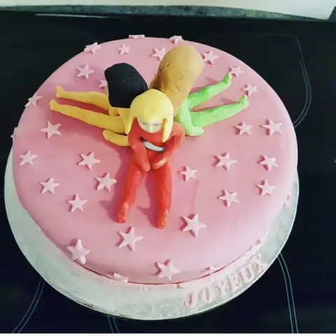 Gâteau rose étoilé où sont allongées trois figurines des Totally Spies en combinaisons rouge, jaune et verte