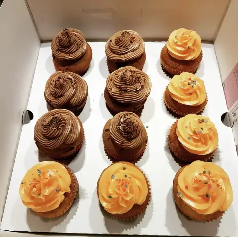 Boîte de douze cupcakes, six à la crème chocolat et vermicelles, six à la crème orange et paillettes colorées