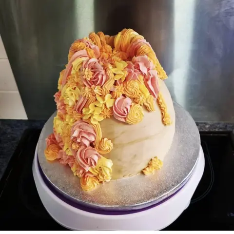 Gâteau en dôme couvert de pâte beige, garni d'une cascade de rosaces de crème roses, orange et jaunes