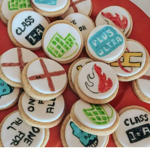 Sablés ronds glacés de blanc, peints de flammes, de croix, de gants verts et d'inscriptions tirées de My Hero Academia