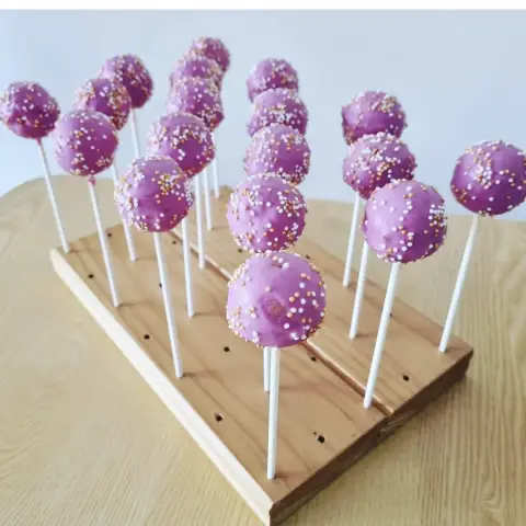 Cake pops enrobés de violet et parsemés de perles blanches et dorées, plantés sur un présentoir en bois