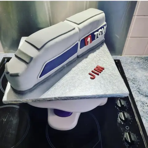 Gâteau en forme de motrice de train gris et bleu, avec un logo rouge sur le flanc et un prénom
