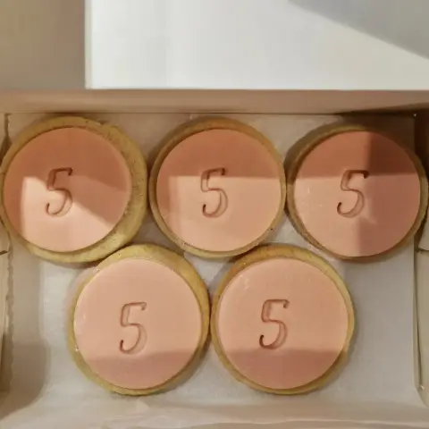 Cinq sablés ronds recouverts de pâte à sucre rose pâle, chacun gravé du chiffre 5