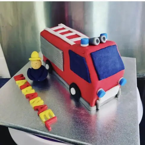 Gâteau camion de pompiers rouge avec échelle et gyrophares bleus, un petit pompier casqué et un prénom