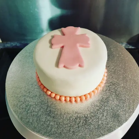 Petit gâteau blanc surmonté d'une croix rose, entouré à sa base d'un rang de perles corail