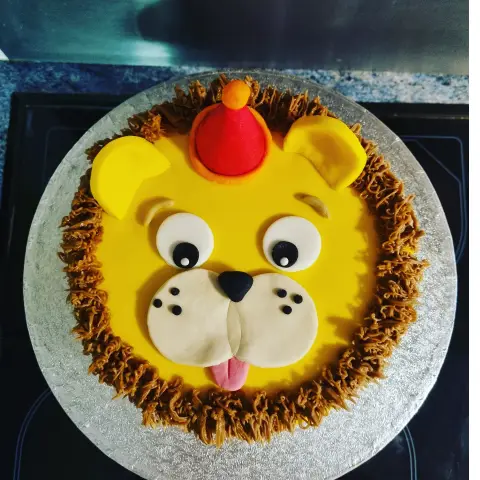 Gâteau rond en tête de lion jaune, à crinière en crème chocolat, langue rose et petit chapeau rouge