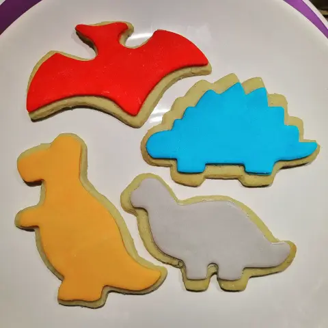 Quatre sablés en forme de dinosaures, recouverts de pâte à sucre rouge, bleue, orange et grise