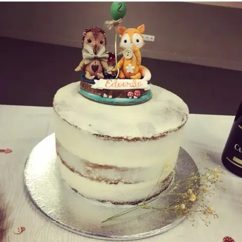 Naked cake blanc surmonté d'un hérisson et d'un renard en sucre, d'un ballon vert marqué 2 et d'un prénom