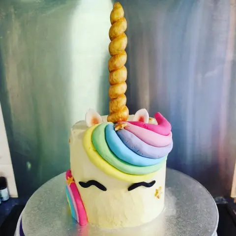 Gâteau blanc aux yeux fermés, à la crinière arc-en-ciel en spirale et à la grande corne dorée torsadée
