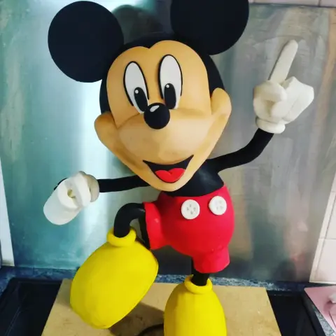 Gâteau sculpté de Mickey debout, en short rouge à boutons blancs et chaussures jaunes, un doigt levé