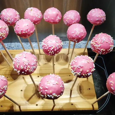 Cake pops enrobés de rose vif et parsemés de vermicelles pastel, piqués sur un présentoir en bois