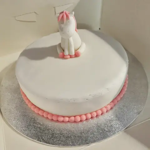 Gâteau blanc bordé de perles roses, surmonté d'un petit cheval blanc assis à la crinière rose