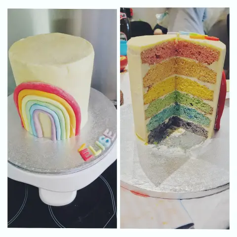 Gâteau blanc orné d'un arc-en-ciel en pâte à sucre, dont la coupe révèle six couches colorées, avec un prénom