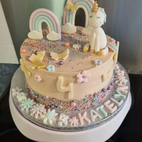 Gâteau pêche à vermicelles avec licorne blanche assise, arcs-en-ciel pastel, papillons dorés, chiffre 4 et un prénom