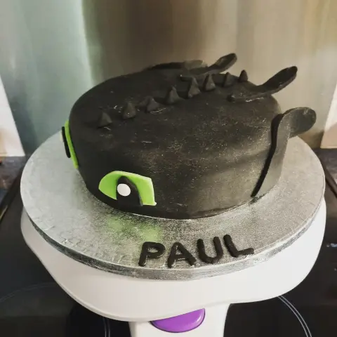 Gâteau noir en forme de Krokmou, avec piques, oreilles et grands yeux verts, et un prénom en lettres noires
