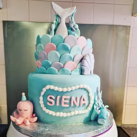 Gâteau turquoise à deux étages, écailles pastel, queue de sirène blanche, coquillage, pieuvre rose et un prénom