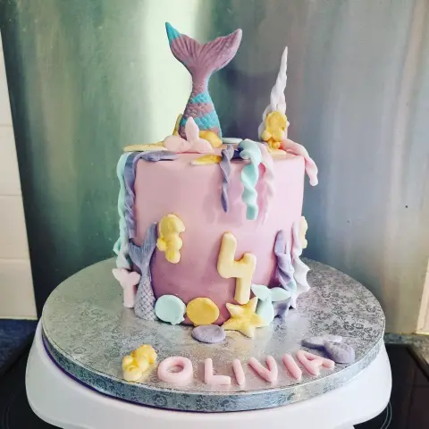 Gâteau rose orné d'algues pastel, de coquillages, d'hippocampes dorés, d'une queue de sirène, du chiffre 4 et d'un prénom