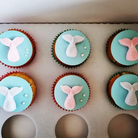 Six cupcakes nappés de turquoise, chacun orné d'une queue de sirène rose ou blanche et de bulles