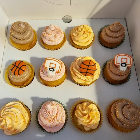Douze cupcakes à crème rose, jaune ou chocolat, parsemés de perles orange, certains ornés de ballons et paniers de basket