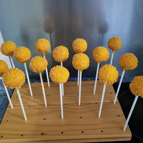 Cake pops enrobés de jaune orangé et couverts de perles orange, piqués sur un support en bois