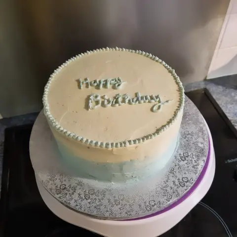 Gâteau à la crème blanche dégradée de bleu ciel, bordé de perles bleues et écrit Happy Birthday