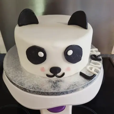 Gâteau blanc en tête de panda aux oreilles et contours des yeux noirs, joues roses, avec un prénom