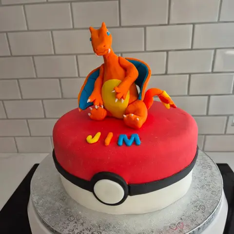 Gâteau en Poké Ball rouge et blanche, surmonté de Dracaufeu et d'un prénom