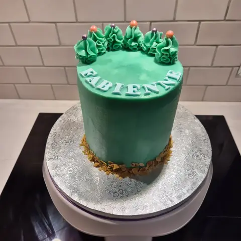 Gâteau haut vert d'eau couronné de volutes de crème et de perles, base d'amandes effilées et prénom bleu clair