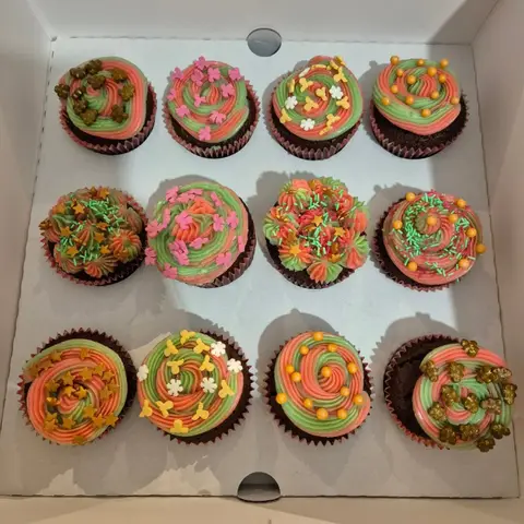 Douze cupcakes au chocolat à crème rose et verte en spirale, décorés d'étoiles dorées, flocons et perles