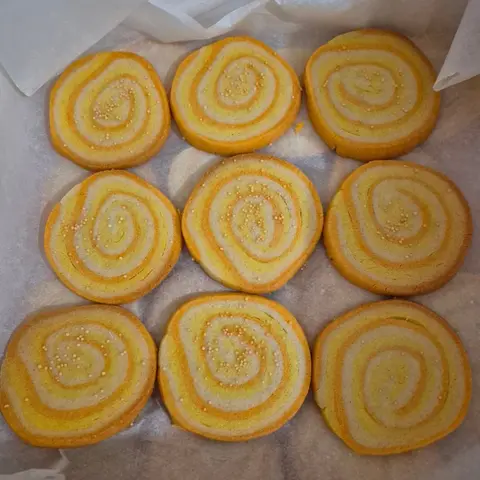 Neuf sablés ronds roulés en spirale jaune, orange et crème, parsemés de petites perles