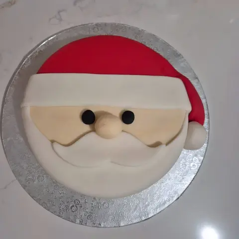Gâteau rond en visage de père Noël, bonnet rouge à pompon blanc, nez rond et grande moustache blanche