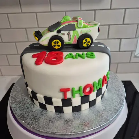 Gâteau blanc à damier noir et blanc, surmonté d'une voiture de course modelée, avec 18 ans et un prénom