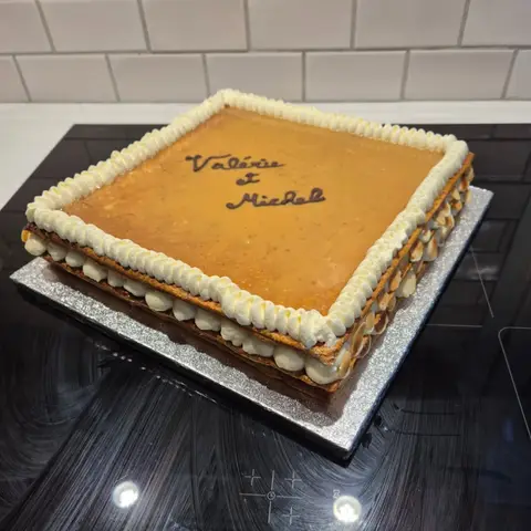 Grand millefeuille carré glacé au caramel, bordé de crème fouettée et d'amandes effilées, deux prénoms écrits au chocolat