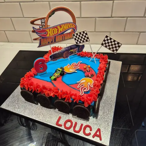 Gâteau carré bleu à piste rouge, petites voitures, flammes et drapeaux à damier, bordé de biscuits au chocolat