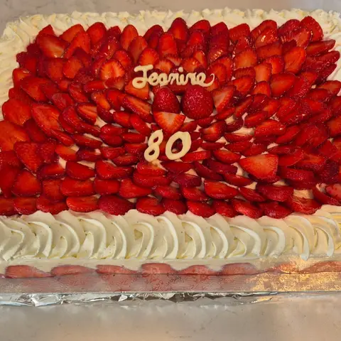 Gros plan sur un fraisier couvert de fraises tranchées, avec un prénom et le nombre 80 en chocolat blanc