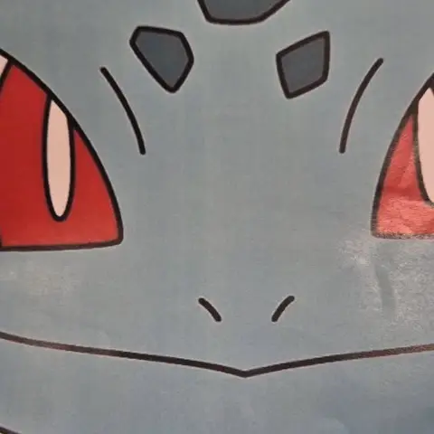 Gros plan sur le visage turquoise de Bulbizarre aux grands yeux rouges et aux taches gris-bleu sur le front