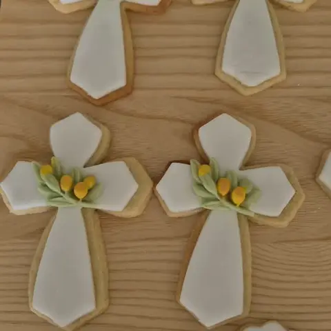 Sablés en forme de croix blanches ornées de feuillage vert et de boutons jaunes, et plaques gravées d'un prénom