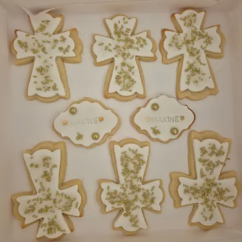 Boîte de sablés en forme de croix glacés de blanc et parsemés de vermicelles dorés, avec deux plaques gravées d'un prénom