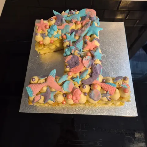 Gâteau en forme de chiffre 1 garni de crème, décoré de queues de sirène, étoiles de mer et coquillages pastel