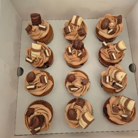 Douze cupcakes à la crème chocolat-noisette, garnis de morceaux de barres chocolatées et d'œufs en chocolat
