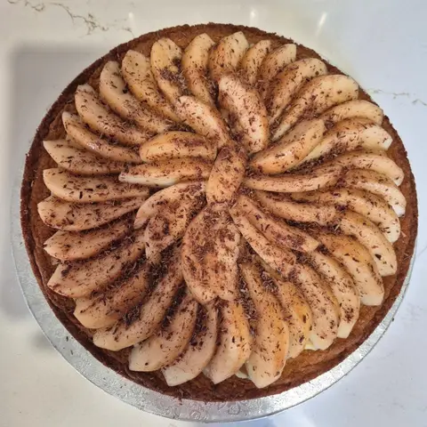 Tarte ronde garnie de lamelles de poire disposées en rosace et parsemées de copeaux de chocolat