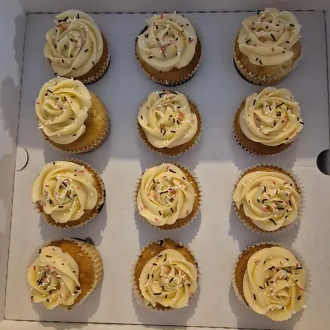 Douze cupcakes coiffés d'une rose de crème vanille et de vermicelles roses, blancs et chocolat