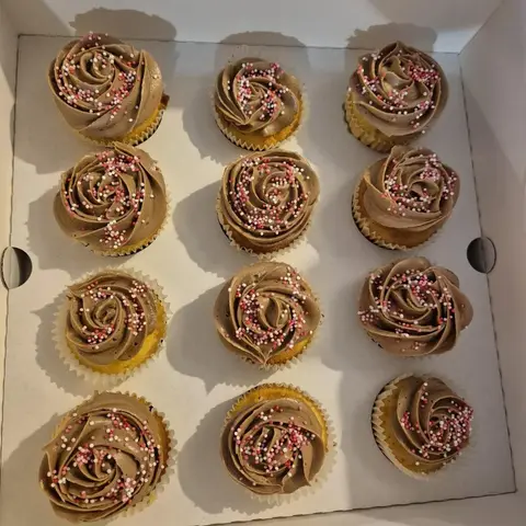 Douze cupcakes coiffés d'une rose de crème au chocolat et de billes de sucre roses et blanches